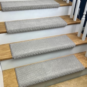 May include: Light gray stair treads with a diamond pattern are installed on wooden stairs. The treads have a soft, textured appearance and are designed to provide a non-slip surface. The stairs have white risers and a wooden handrail.