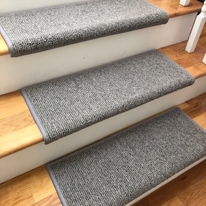 May include: Gray carpet stair treads with a textured surface. The treads are installed on wooden stairs with white risers.