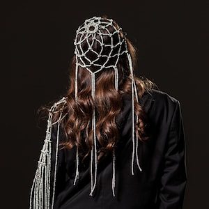 May include: A person wearing a black blazer and trousers, adorned with a silver beaded headpiece and shoulder decoration. The headpiece is a net-like structure, and the shoulder piece features long beaded strands.