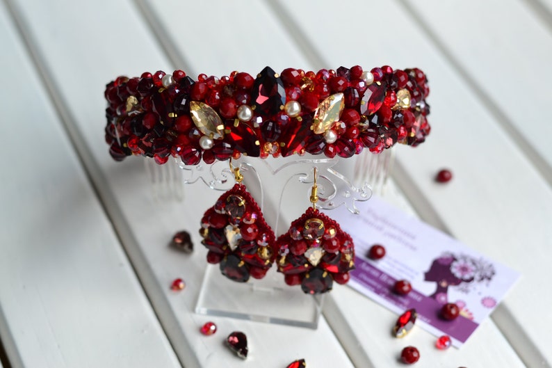 May include: A red and gold beaded headband and matching earrings. The headband has a comb attachment and the earrings are teardrop shaped.