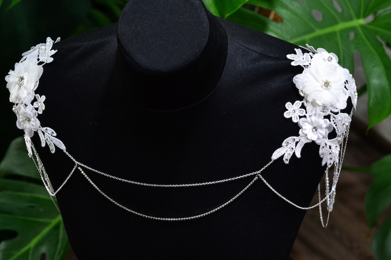 May include: White lace shoulder straps with delicate floral embellishments and a silver chain detail.