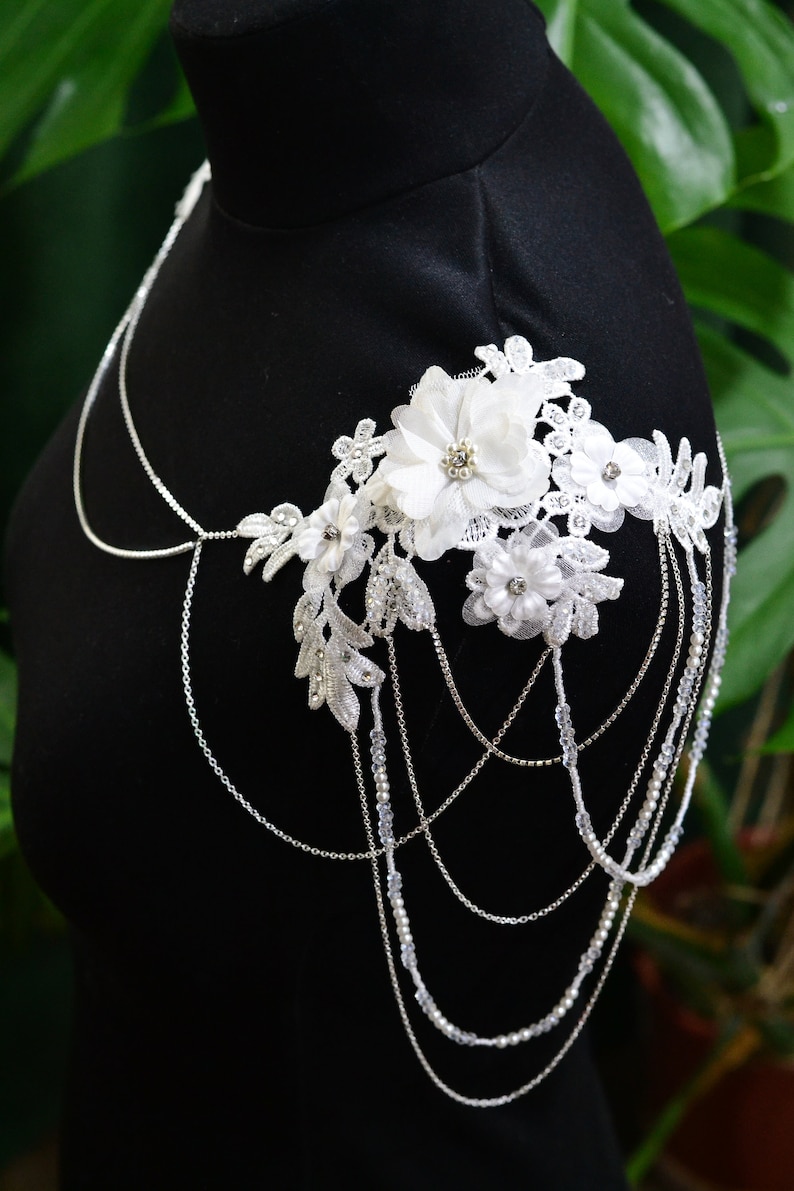 May include: A white lace and silver chain bridal shoulder necklace with delicate floral embellishments.
