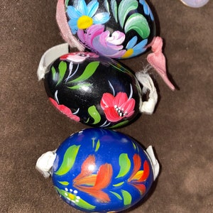 Può includere: Tre uova di legno dipinte a mano con motivi floreali. L'uovo superiore è nero con fiori rosa, blu e verdi. L'uovo centrale è nero con fiori rossi e bianchi. L'uovo inferiore è blu con fiori arancioni e bianchi.