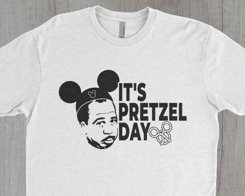 K&ouml;nnte beinhalten: Wei&szlig;es T-Shirt mit einer schwarz-wei&szlig;en Grafik einer Person mit Mickey-Mouse-Ohren und dem Text "It's Pretzel Day".