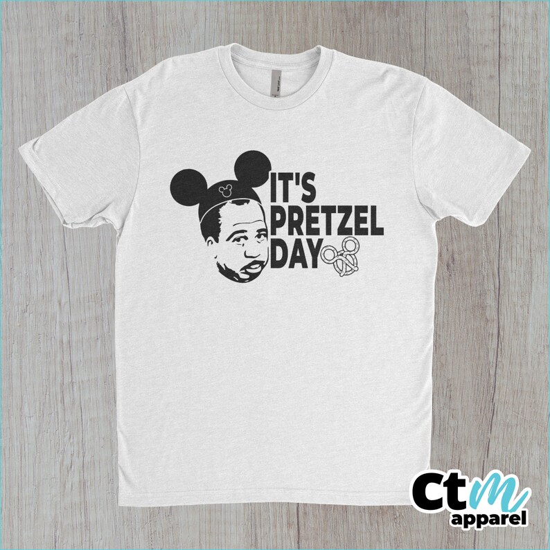 K&ouml;nnte beinhalten: Wei&szlig;es T-Shirt mit einer schwarz-wei&szlig;en Grafik einer Person mit Mickey-Mouse-Ohren und dem Text "It's Pretzel Day".