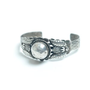 May include: A silver bracelet with a round, raised, silver centre piece and intricate, detailed designs on the sides.