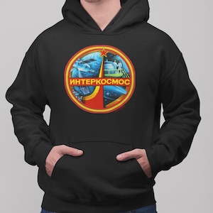 May include: Black hooded sweatshirt with a red, yellow, and blue circular graphic featuring a red star and the text "ИНТЕРКОСМОС".