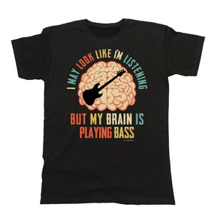 May include: Black t-shirt with a vintage-style graphic of a brain with a bass guitar inside. The text reads "I may look like I'm listening but my brain is playing bass".