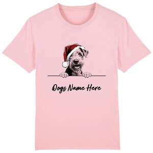 Puede incluir: Camiseta rosa claro con un perro con un gorro de Papá Noel. La ilustración del perro es en blanco y negro, con el texto "Dogs Name Here" debajo.