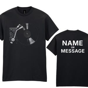 May include: Black t-shirt with a grayscale record player graphic on the front. The back of the shirt has the white text "NAME OR MESSAGE". A simple design for music enthusiasts.
