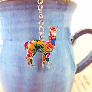 Peut inclure: Un charme de thé en forme de lama coloré suspendu à une chaîne argentée. Le lama est en métal et présente un design détaillé avec des couleurs vives, notamment le jaune, le rouge, le bleu, le vert et le rose.