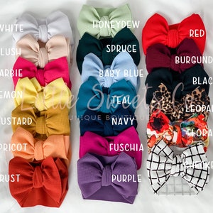 May include: A collection of baby headbands in various colors, including white, blush, red, and leopard print. Each headband features a large bow. The image includes the text "Little Sweet Unique Boutique".