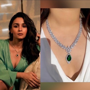 May include: A silver necklace with a large green gemstone pendant. The necklace is made of small, clear stones that are set in a leaf-like pattern. The pendant is a teardrop shape and is surrounded by smaller stones.