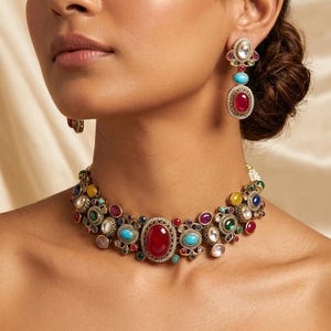 Könnte beinhalten: Ein goldfarbenes Halsketten- und Ohrring-Set. Die Halskette hat einen großen roten ovalen Stein in der Mitte, umgeben von kleineren bunten Steinen. Die Ohrringe haben ein ähnliches Design mit roten und türkisfarbenen Steinen.