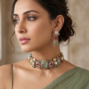May include: A gold-toned choker necklace and matching drop earrings featuring an intricate metalwork design. The jewelry is set with various oval and round cabochon gemstones in shades of sage green, deep red, blue, and cream, arranged in a pattern.