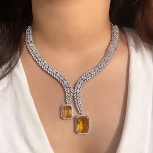May include: A silver necklace with a delicate chain design and two large, rectangular, yellow gemstones. The necklace has a V-shaped neckline and a dangling design.