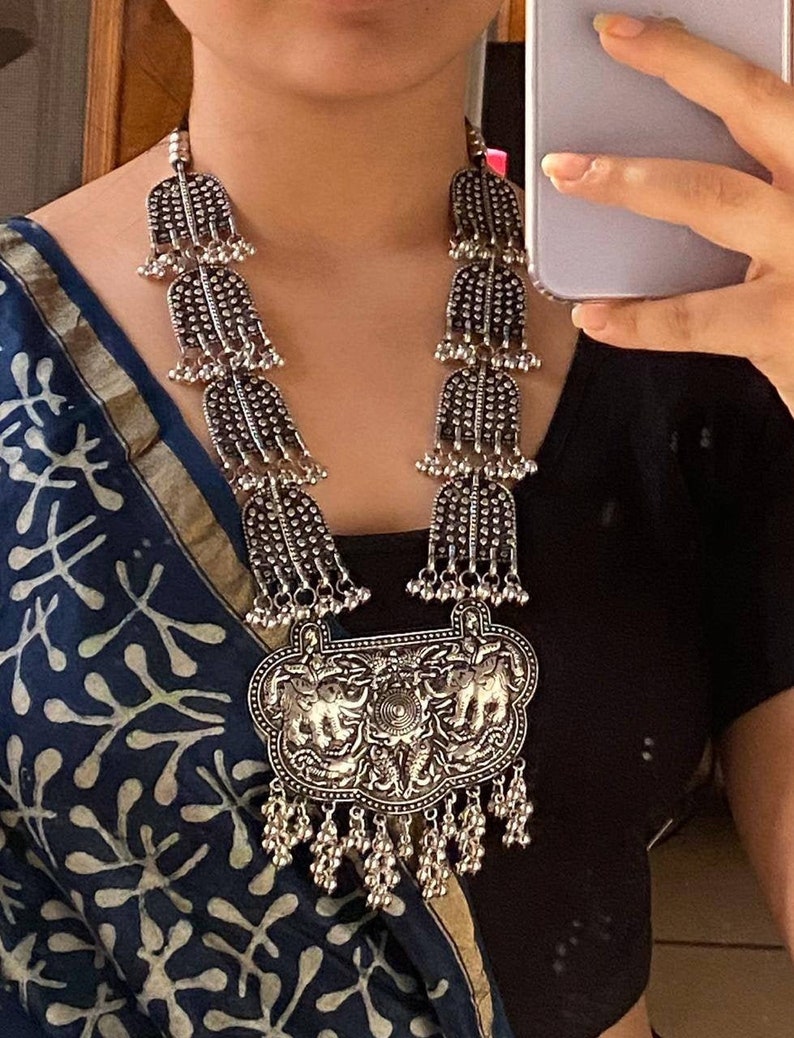 May include: A silver necklace with a large pendant featuring two elephants. The pendant is surrounded by smaller silver beads and hangs from a chain of silver beads.