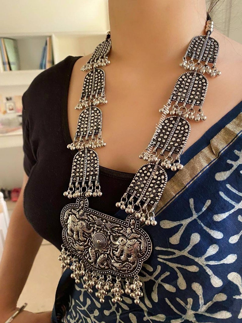 May include: A silver necklace with a large pendant featuring three elephants. The pendant is surrounded by smaller silver beads and hangs from a chain of silver beads and decorative silver pieces.