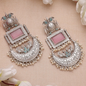 May include: Silver earrings with a pink stone, a crescent moon design, and pearl accents.