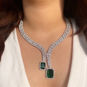 May include: A silver necklace with a layered chain design and two emerald green gemstone pendants.