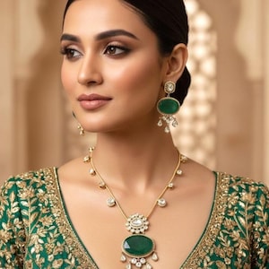 May include: A woman wearing a gold necklace and matching earrings. The jewelry features large, oval, emerald-green stones and smaller clear stones. The woman is wearing a green top with gold embroidery.