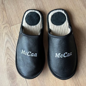May include: A pair of black leather slippers with white embroidered text that reads "McCaа".