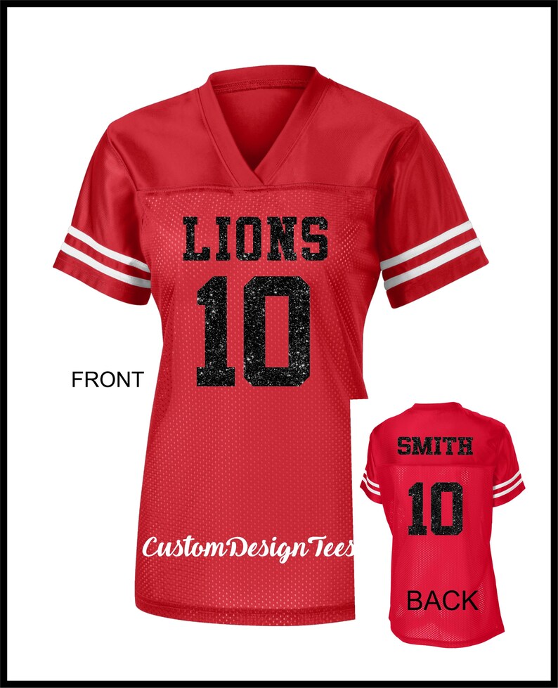 May include: A red V-neck jersey with short sleeves featuring two white stripes on each sleeve. The front displays the word LIONS and the number 10 in black glitter. The back shows the name SMITH and the number 10 in black glitter text.