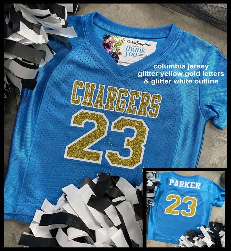 May include: A Columbia blue jersey with gold glitter lettering that reads "CHARGERS" and the number "23". The jersey has a white glitter outline. The image also includes a smaller jersey with the name "PARKER" and the number "23".