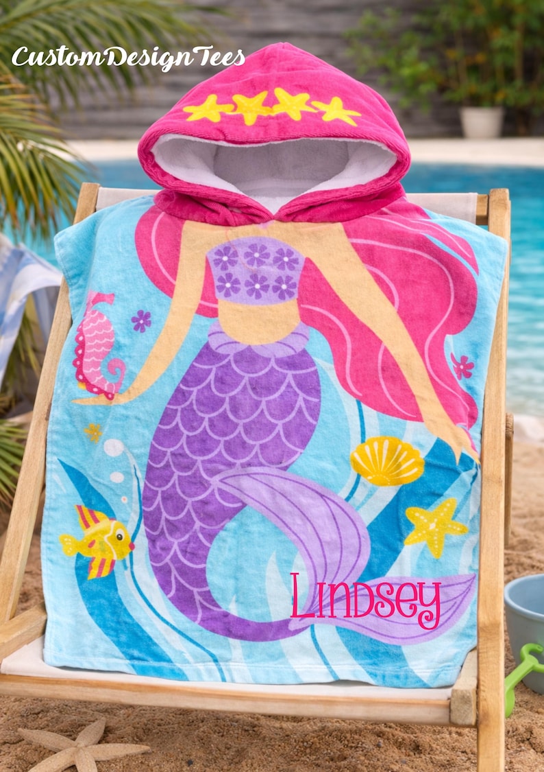 Pode incluir: Uma toalha de praia com capuz com um design de sereia. A toalha &eacute; azul com uma cauda de sereia roxa e cabelo rosa. O capuz &eacute; rosa com detalhes de estrelas amarelas. O nome "Lindsey" est&aacute; impresso na toalha. O texto "Custom Design Tees" est&aacute; no topo.
