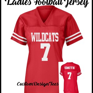 May include: A red V-neck football jersey with white stripes on the sleeves. The front features the text WILDCATS and the number 7 in white. A smaller inset shows the back of the jersey with the name SMITH and the number 7 in white lettering.