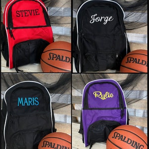 May include: Four personalized basketball backpacks with a basketball in front of each. The backpacks are red, black, black, and purple. The names on the backpacks are Stevie, Jorge, Maris, and Rylie.