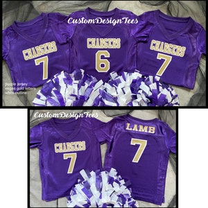 May include: Purple football jerseys with gold lettering and white outlines. The jerseys display the word "CHARGERS" and the numbers 6 and 7. The image also includes white and purple pom-poms. The text "Custom Design Tees" is visible.