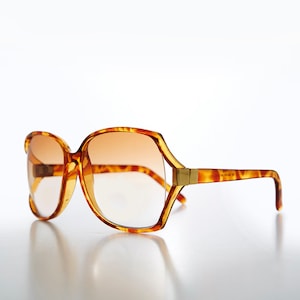 May include: Tortoiseshell sunglasses with brown lenses. The sunglasses have a gold accent on the side.