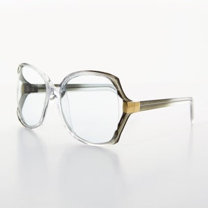 Puede incluir: Gafas con montura de plástico transparente con detalles dorados en las patillas. Las gafas tienen un estilo retro.