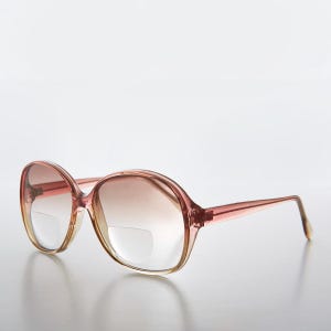 May include: A pair of pink and clear plastic oval-shaped reading glasses with a gradient brown tint.