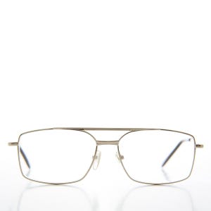 May include: Silver-toned eyeglasses with a double bridge and rectangular lenses. The frames have a thin, minimalist design. The glasses are set against a white background.