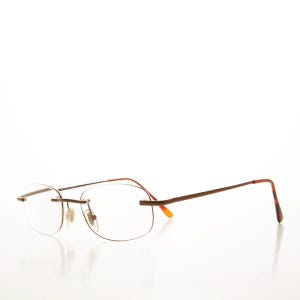 May include: Rimless spectacles with a brown metal frame and clear lenses. The temples have a tortoiseshell pattern at the ends. The glasses have a minimalist design.