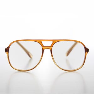 Puede incluir: Un par de gafas de estilo vintage con montura marrón claro. Las gafas tienen un doble puente y lentes grandes y transparentes. La montura es de color ámbar cálido, y el diseño recuerda a las gafas de aviador.