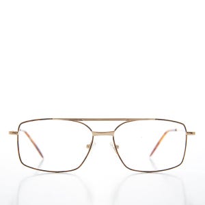 May include: Gold-tone metal eyeglasses with a double bridge and rectangular lenses. The frames have a thin, delicate design with a classic aviator style. The lenses have a slight tint.