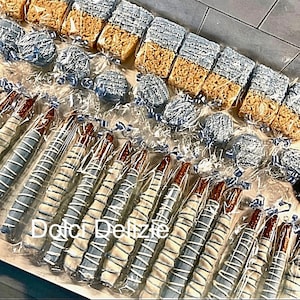 May include: An assortment of treats, including chocolate-covered pretzels, Rice Krispie treats, and cake pops, all decorated in blue and white. The pretzels are wrapped in clear cellophane, and the image includes the text "Dolo Delizie".