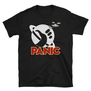 Peut inclure: T-shirt noir avec un graphique blanc d'une main tenant une planète avec le mot "PANIC" en lettres rouges en dessous. Trois soucoupes volantes sont représentées au-dessus de la planète.