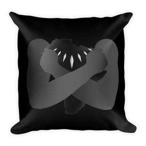 May include: Black and white throw pillow with a silhouette of a person's arms crossed over their chest, forming the shape of the continent of Africa. The person is wearing a necklace with five points.