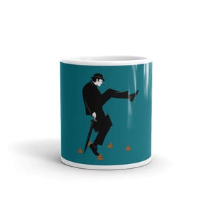 May include: A white ceramic mug with a teal blue background featuring a black and white illustration of a man in a suit and bowler hat kicking a pile of brown poo. The man is holding an umbrella and a briefcase.