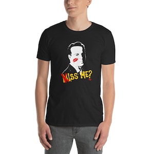 May include: Black t-shirt with a white silhouette of a man with a red lipstick mark on his cheek. The text "Kiss Me?" is written in yellow and red paint.