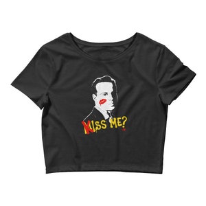 Puede incluir: Camiseta negra de corte corto con una silueta blanca de un hombre con una marca de lápiz labial rojo en la mejilla. El texto "Kiss Me?" está escrito en letras amarillas y rojas debajo de la imagen.