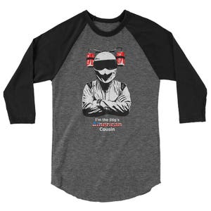 Könnte beinhalten: Ein graues und schwarzes Baseball-T-Shirt mit einem weißen Bild einer Person, die einen Helm trägt und ein Lenkrad hält. Der Text "I'm the Stig's American Cousin" ist auf dem Shirt aufgedruckt.