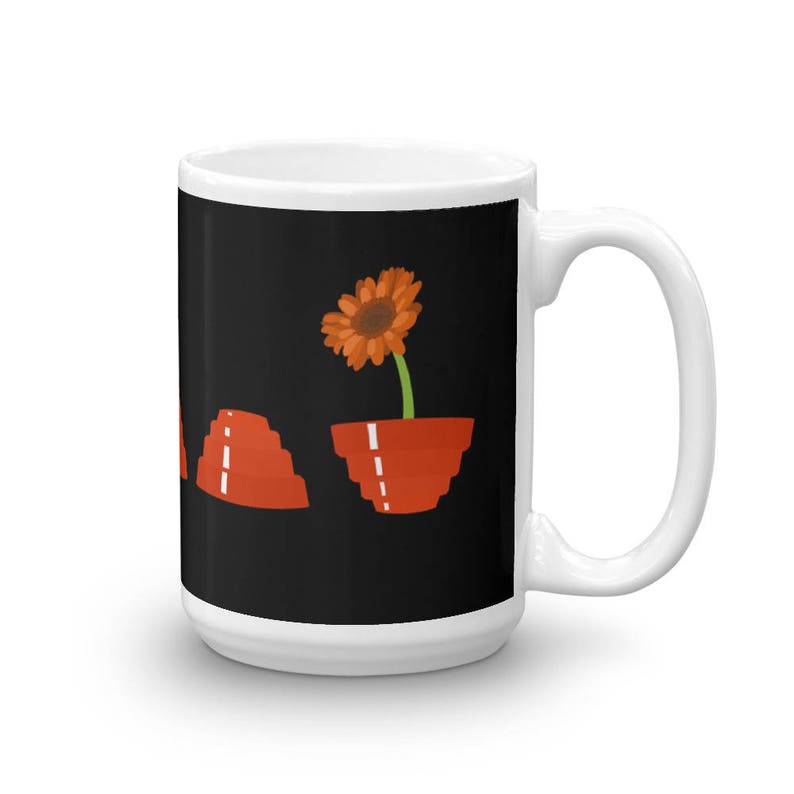 May include: White ceramic mug with a black background featuring a single orange flower in a red pot. The flower is growing out of the pot and has a green stem. There are three red stacked cups on the left side of the mug.