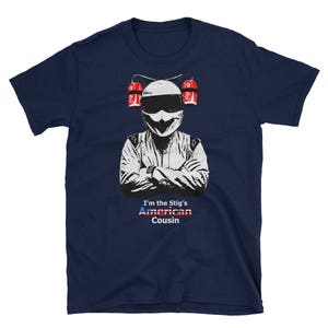 Könnte beinhalten: Ein marineblaues T-Shirt mit einer weißen Grafik einer Person, die einen Rennhelm trägt und zwei rot-weiße Dosen hält. Der Text "I'm the Stig's American Cousin" ist unter der Grafik gedruckt.