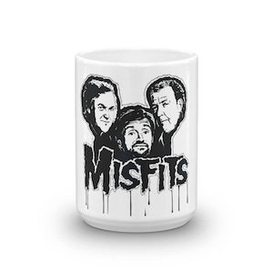 Op de afbeelding: Witte keramische mok met een zwart-witte illustratie van drie mannengezichten en het woord "MISFITS" in druipende zwarte verf.
