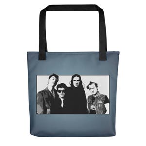 Può includere: Una borsa tote blu con manico nero e un'immagine in bianco e nero di una band. I membri della band indossano abiti scuri e hanno un'espressione seria.